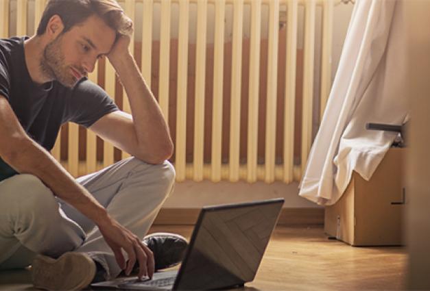 sad Young male adult sitting on floor looking at laptop computer 