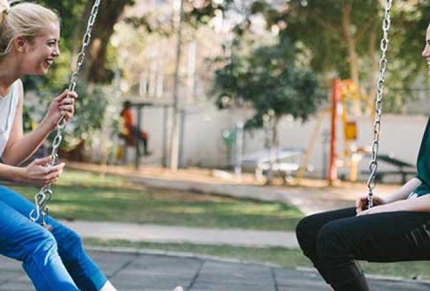 Two young women sitting on swings chatting