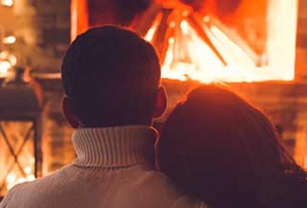 a couple dressed warmly in front of a fire in a fireplace snuggle close together