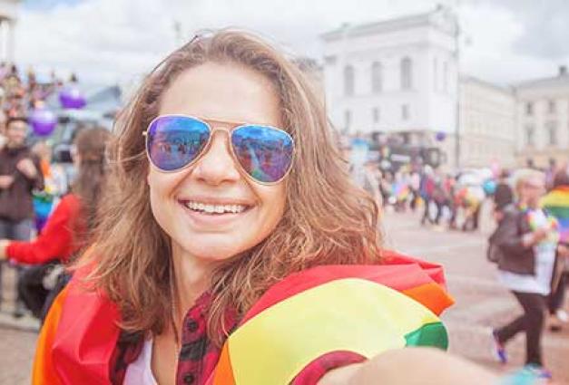 young happy woman with a rainbow flag takes a selfie on a mobile phone at a pride event
