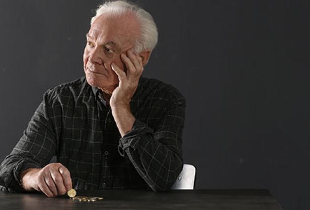 elderly man with coins sitting at table on dark background