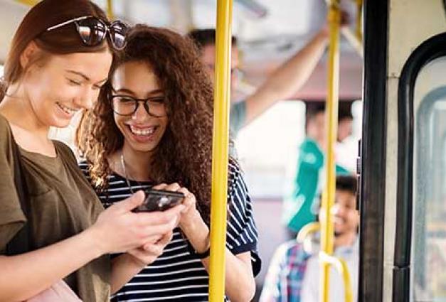 Two young woman chat and look at phone on bus