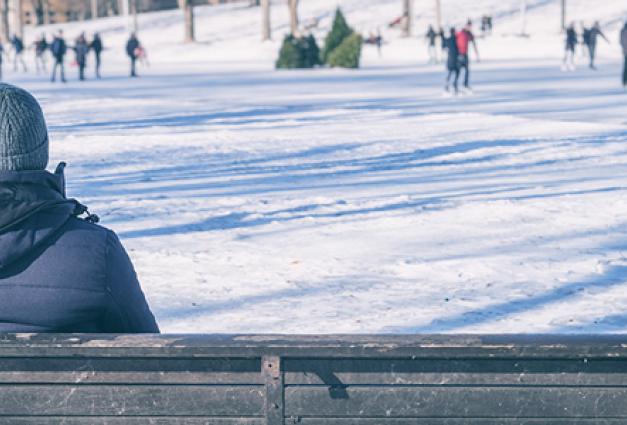 Man sitting on bench looking at people ice skating