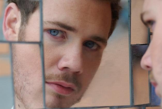 Blonde hair blue eyed man looking into shattered mirror