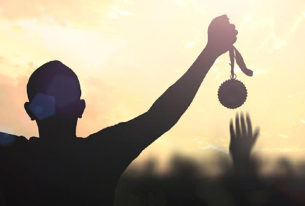 Silhouette of a man hand holding a third place medal against colorful sunset sky