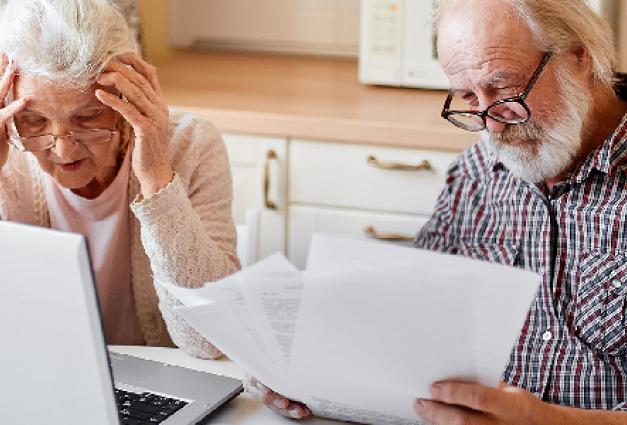 Mature couple sitting at kitchen table with laptop looking through financial papers,