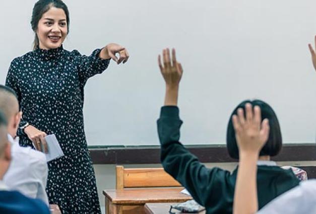 A smiling female high school teacher in front of students in classroom