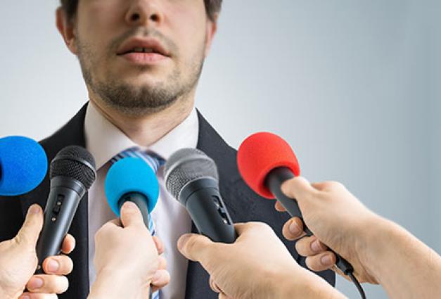 Man giving interview to reporters with microphones in front