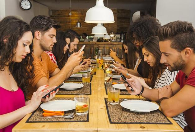 Image of young men and women sitting around a table on their smartphones
