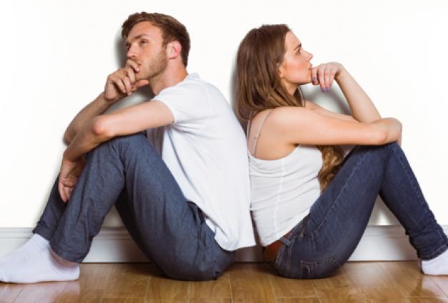 Image of man and woman sitting on floor, back-to-back, thinking 