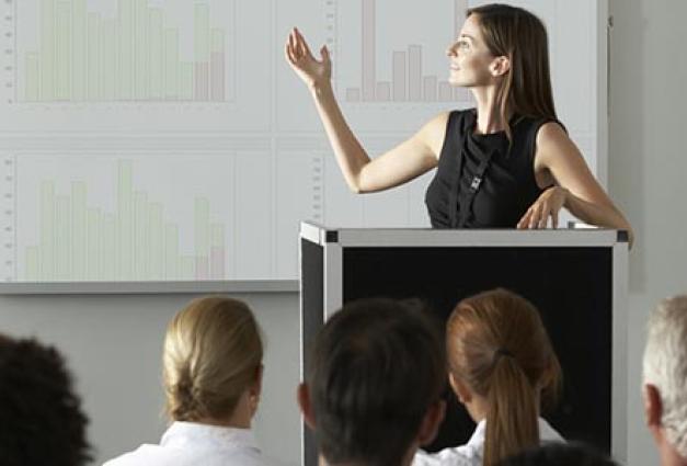 Woman stands at podium, presenting research to an small audience at a conference
