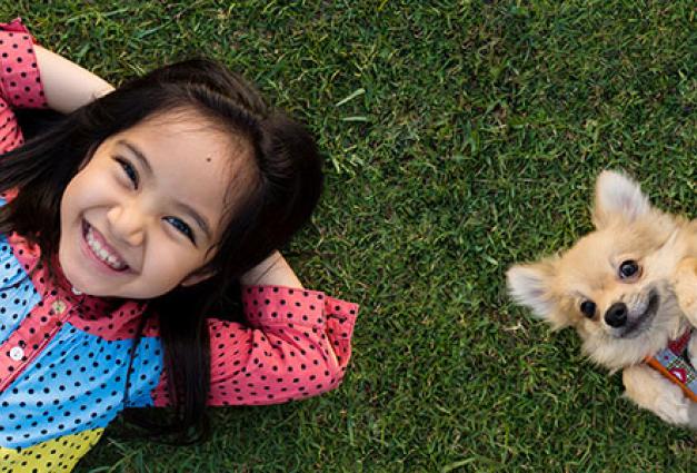 Young Asian girl lying on grass with her small dog