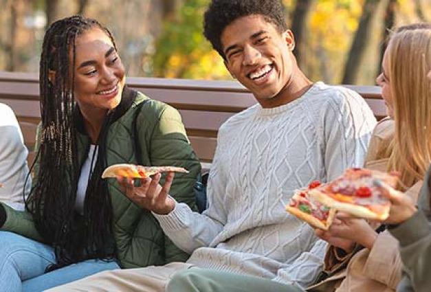 Group of young adults eating pizza on bench