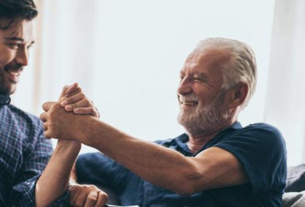 Cheerful elderly man sitting on next to younger man embracing hands